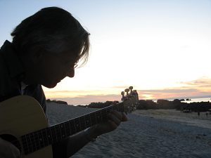 Christian Straube im Gegenlicht spielt gitarre am Strand